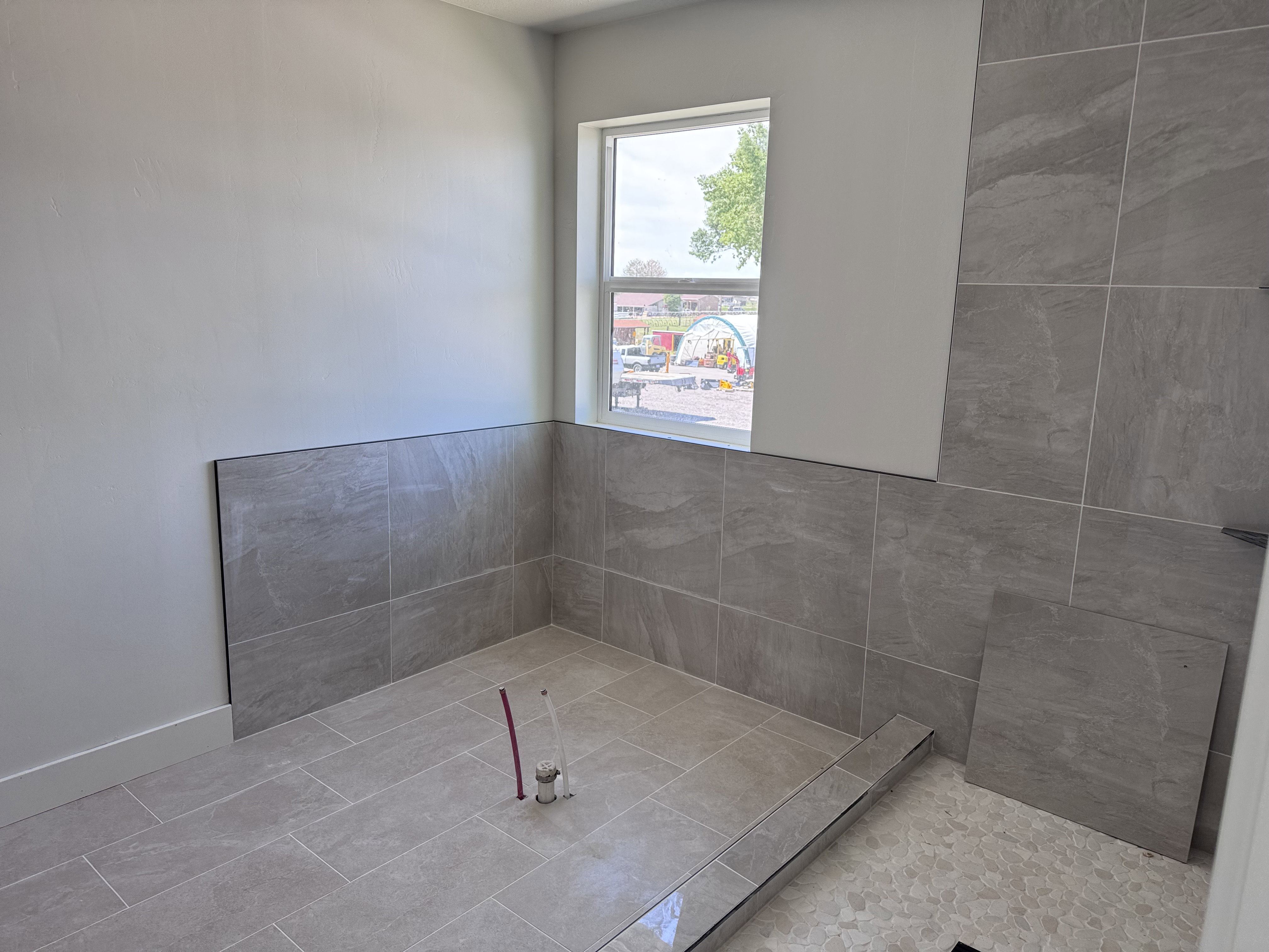Shower area featuring large format gray tile on walls and floor, a linear drain, and a window with trim