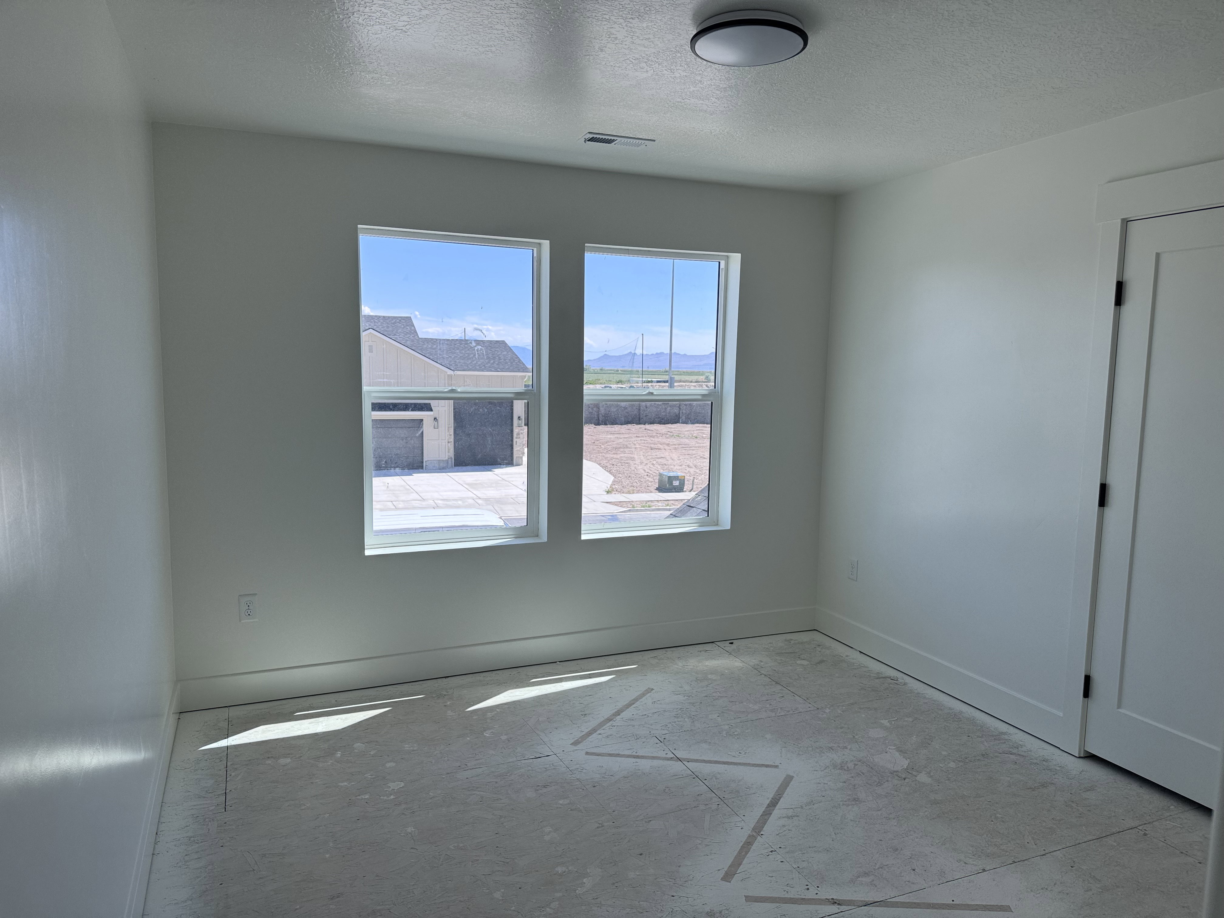 Bright interior space featuring two windows, a contemporary flush-mount ceiling light fixture, baseboard trim, and a paneled interior door