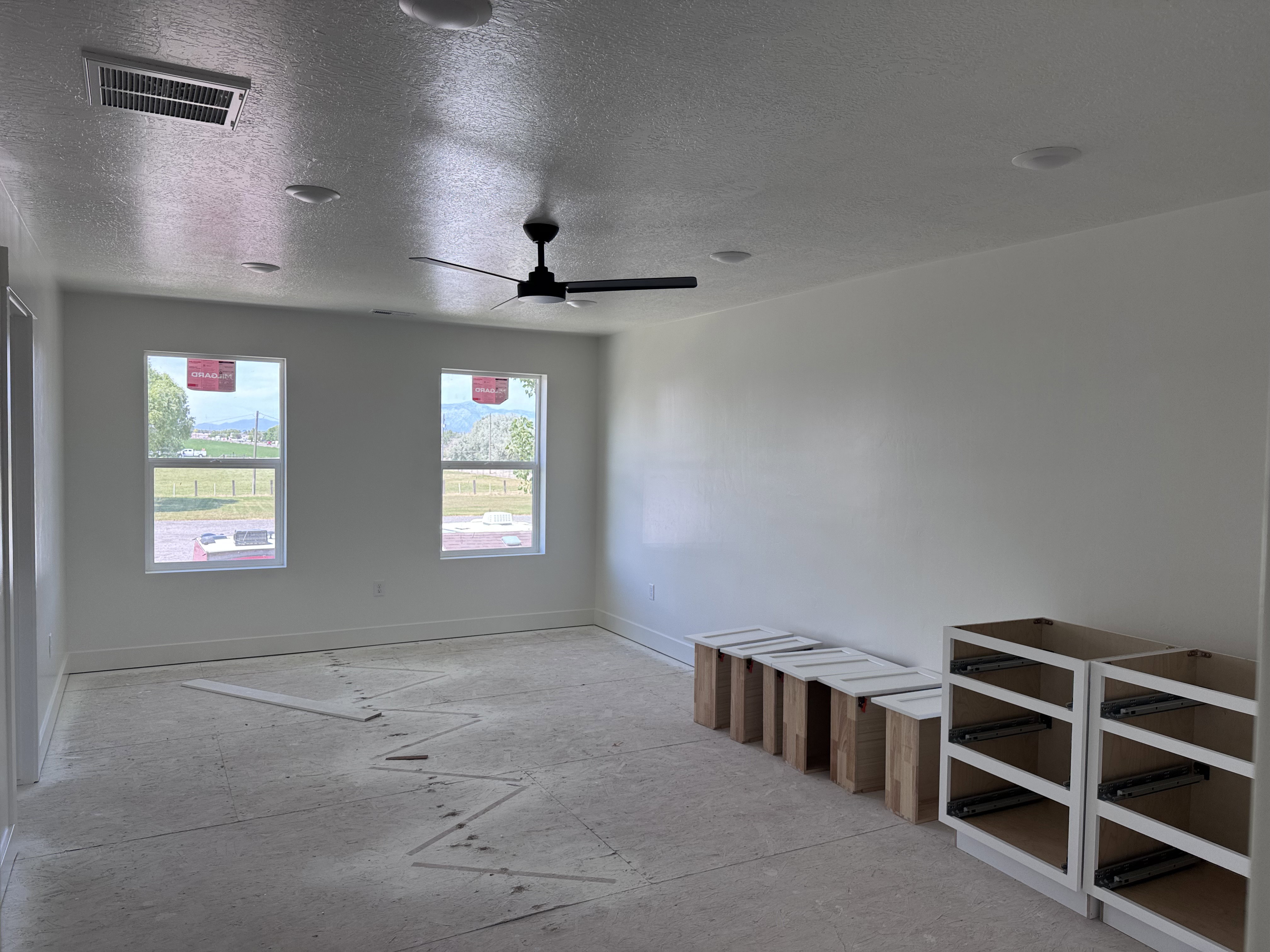 Spacious room with white walls, two large windows, a ceiling fan, and recessed lighting