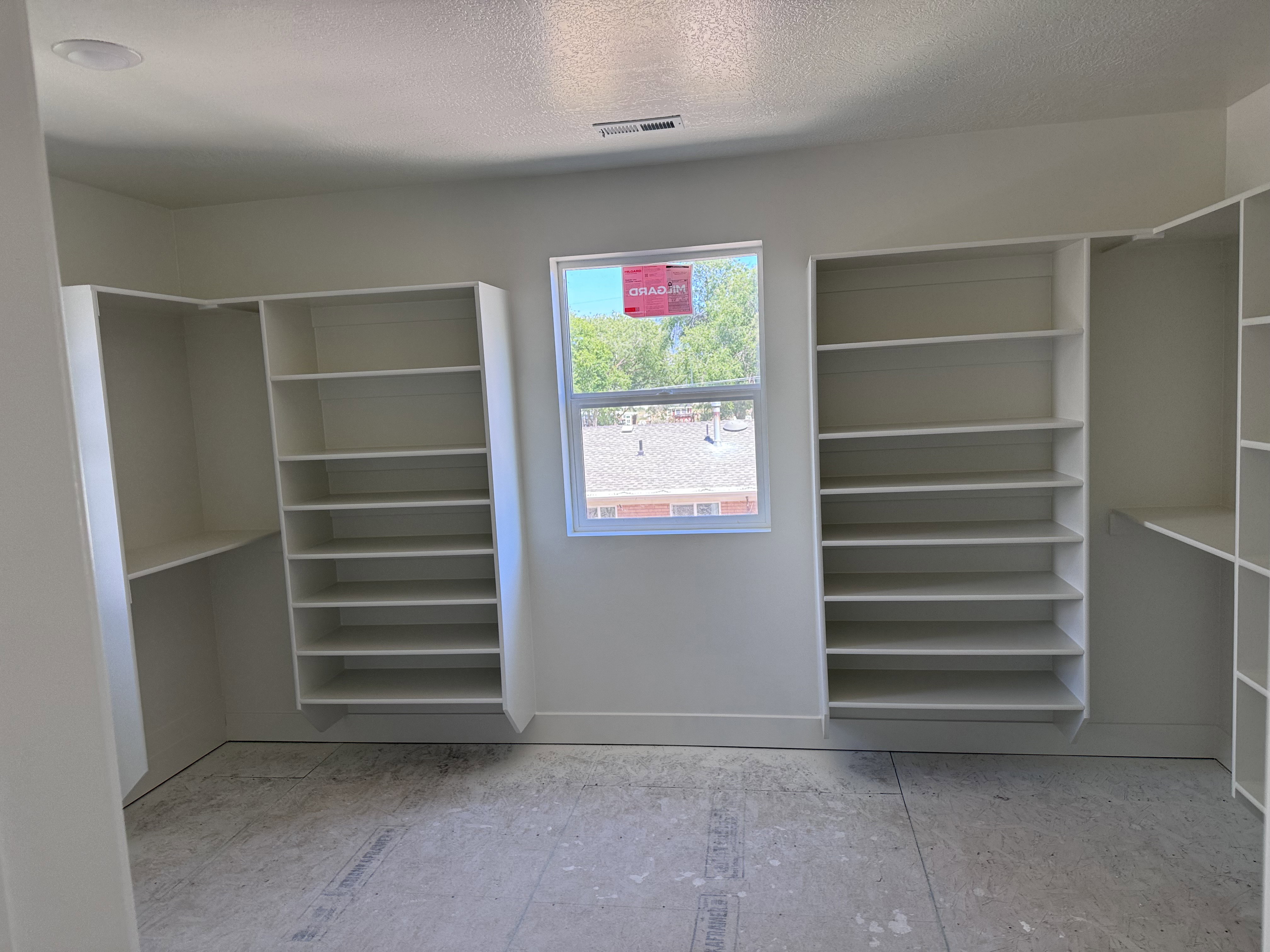 Spacious room featuring multiple built-in shelving units, a recessed ceiling light, a window providing natural light, and a vent