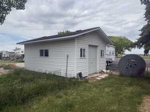 Freestanding outbuilding featuring white horizontal siding, a dark shingle roof, and a single garage door