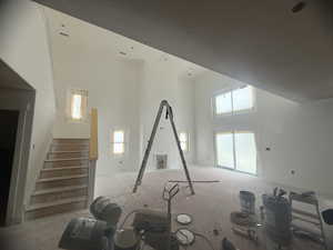 Two-story great room featuring high ceilings, a prominent staircase with unfinished wood newel post, and multiple windows including a large sliding glass door