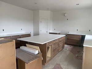 Spacious kitchen featuring a large central island, perimeter cabinetry with a wood finish, crisp white countertops, and recessed ceiling lighting