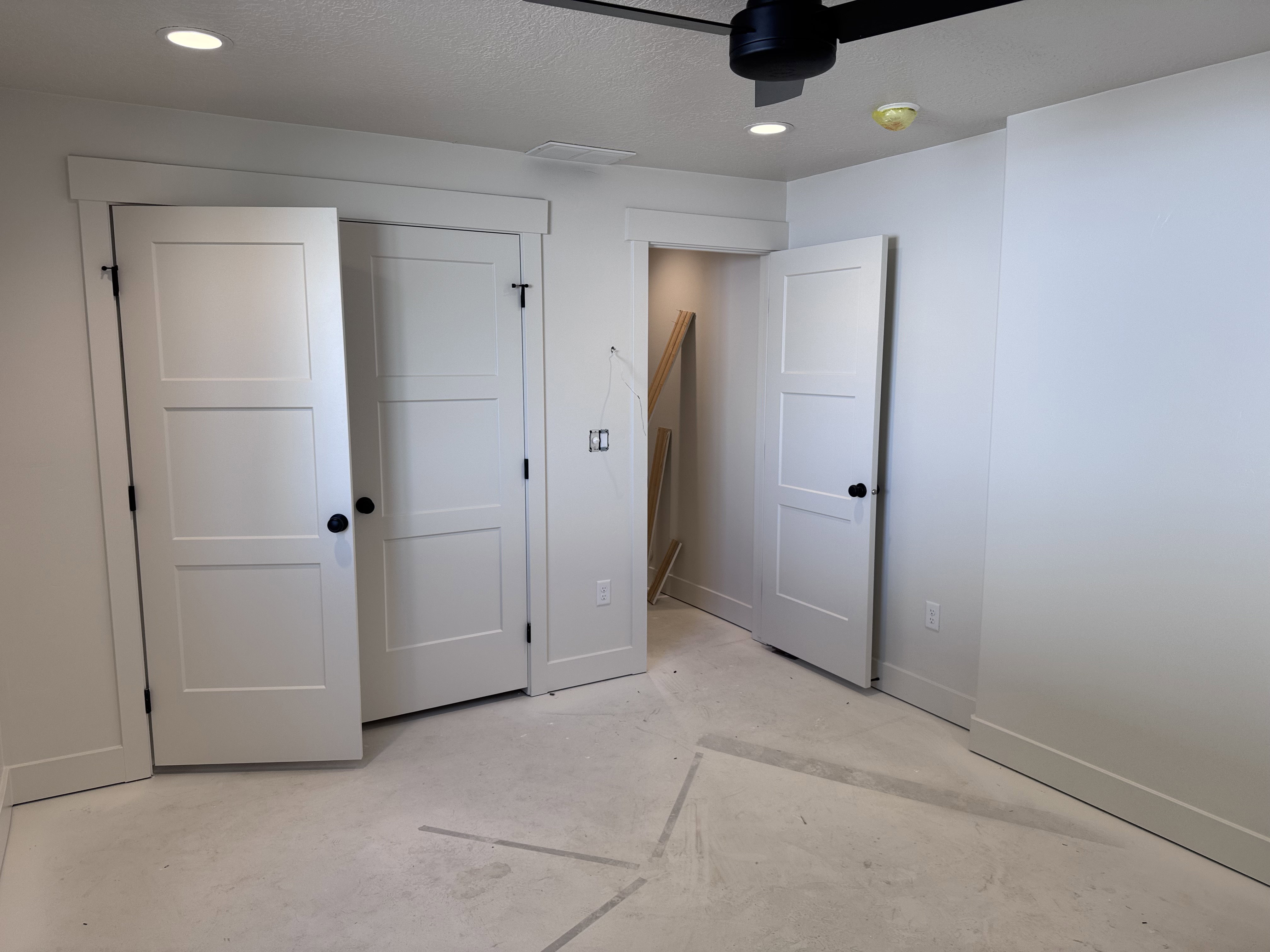 Interior room featuring white walls, three-panel interior doors with matte black hardware, recessed ceiling lighting, and a black ceiling fan