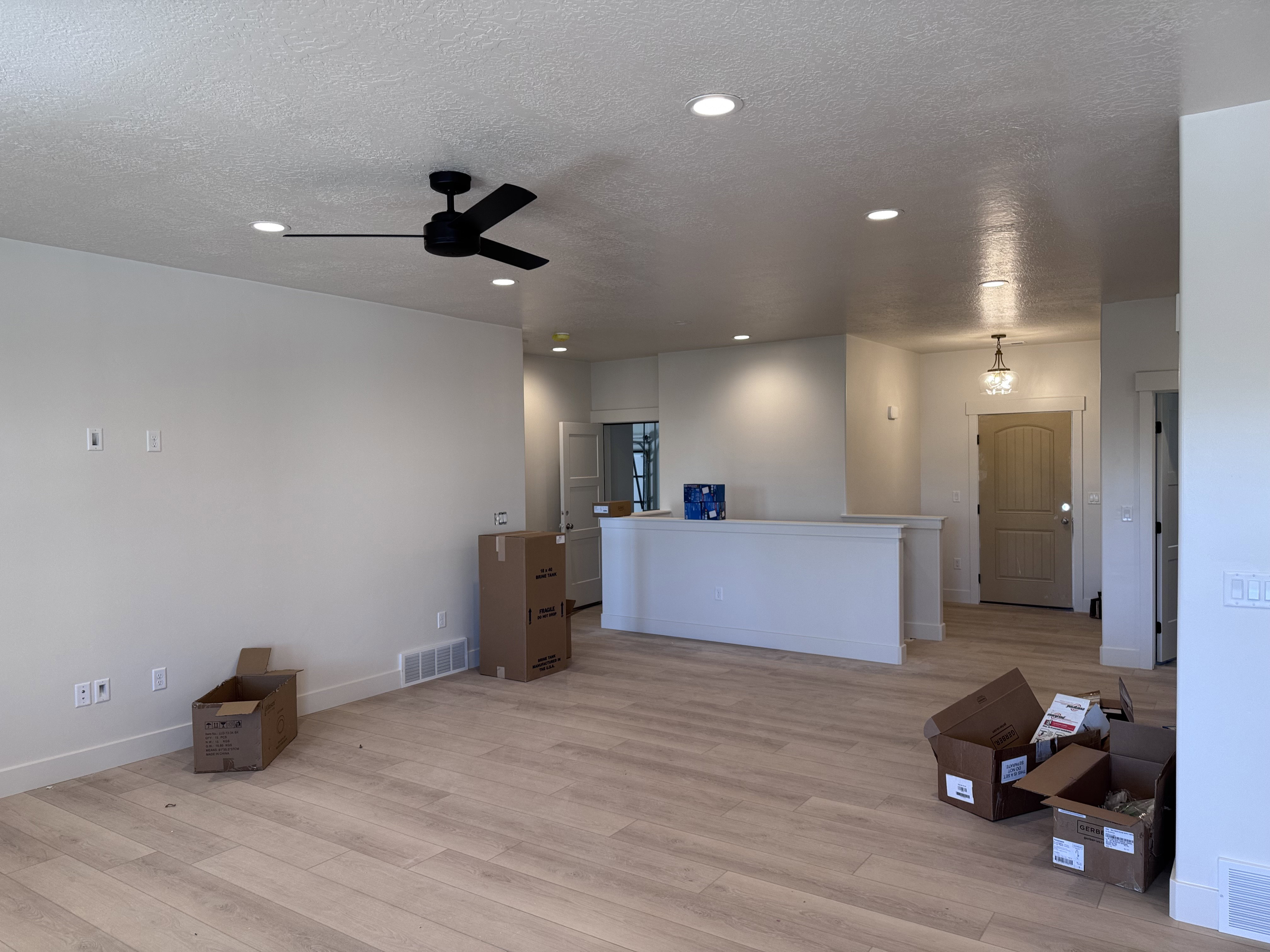 Spacious open-concept room featuring light wood-finish flooring, recessed lighting, and a modern black ceiling fan
