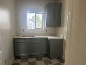 Utility area featuring a stainless steel sink, light-toned countertop, and green shaker-style cabinetry