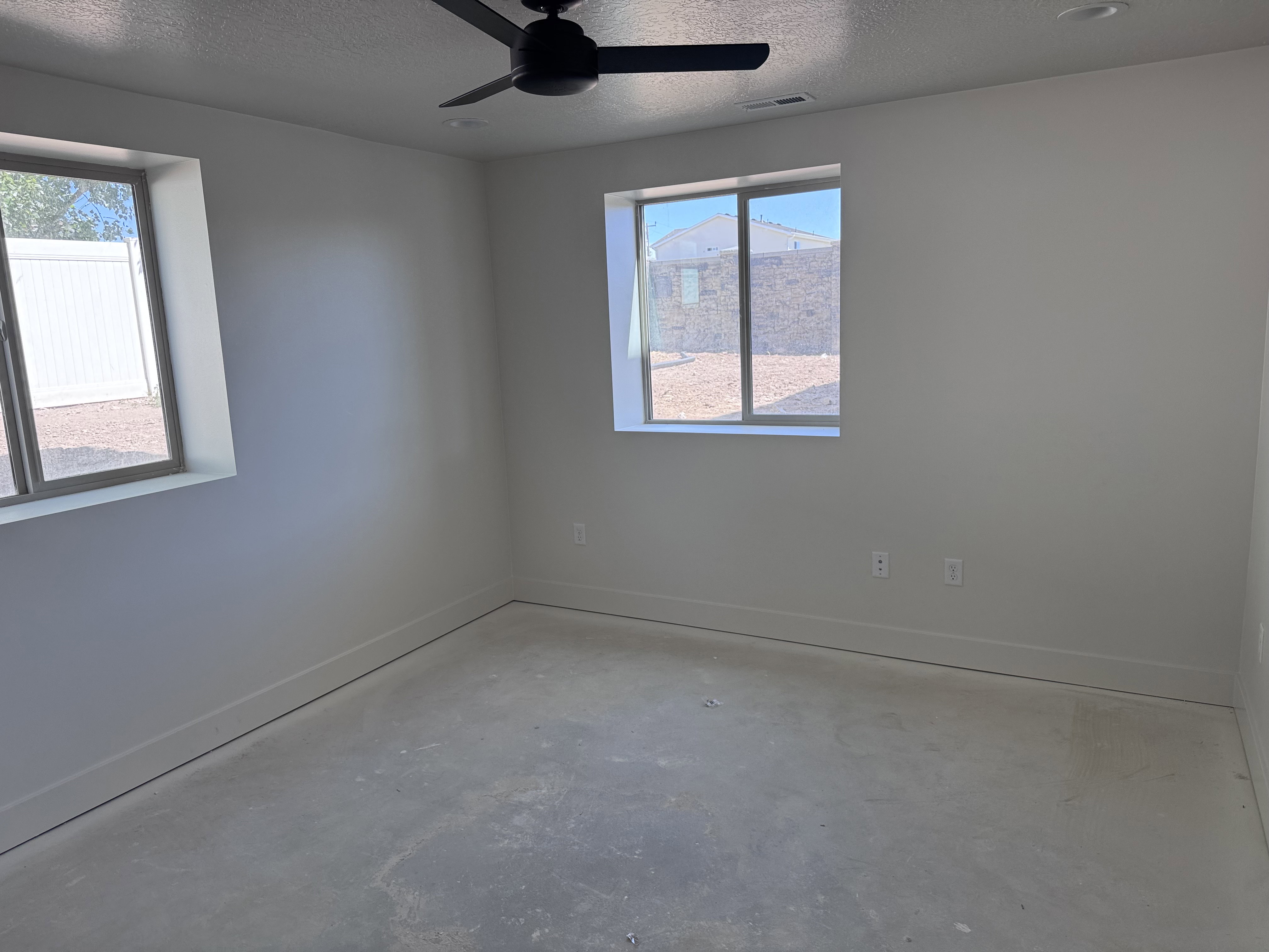 Unfinished room featuring two windows with white trim, a ceiling fan with integrated lighting, and recessed ceiling lighting