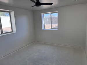 Unfinished room featuring two windows with white trim, a ceiling fan with integrated lighting, and recessed ceiling lighting