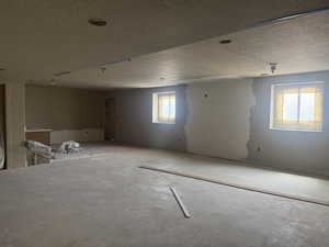 Spacious unfinished room featuring concrete flooring, two windows, recessed lighting, and a partial built-in cabinet base