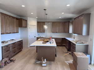 Spacious kitchen featuring extensive cabinetry, light-toned wood-finish flooring, recessed lighting, a central island with pendant lighting, and light-toned countertops