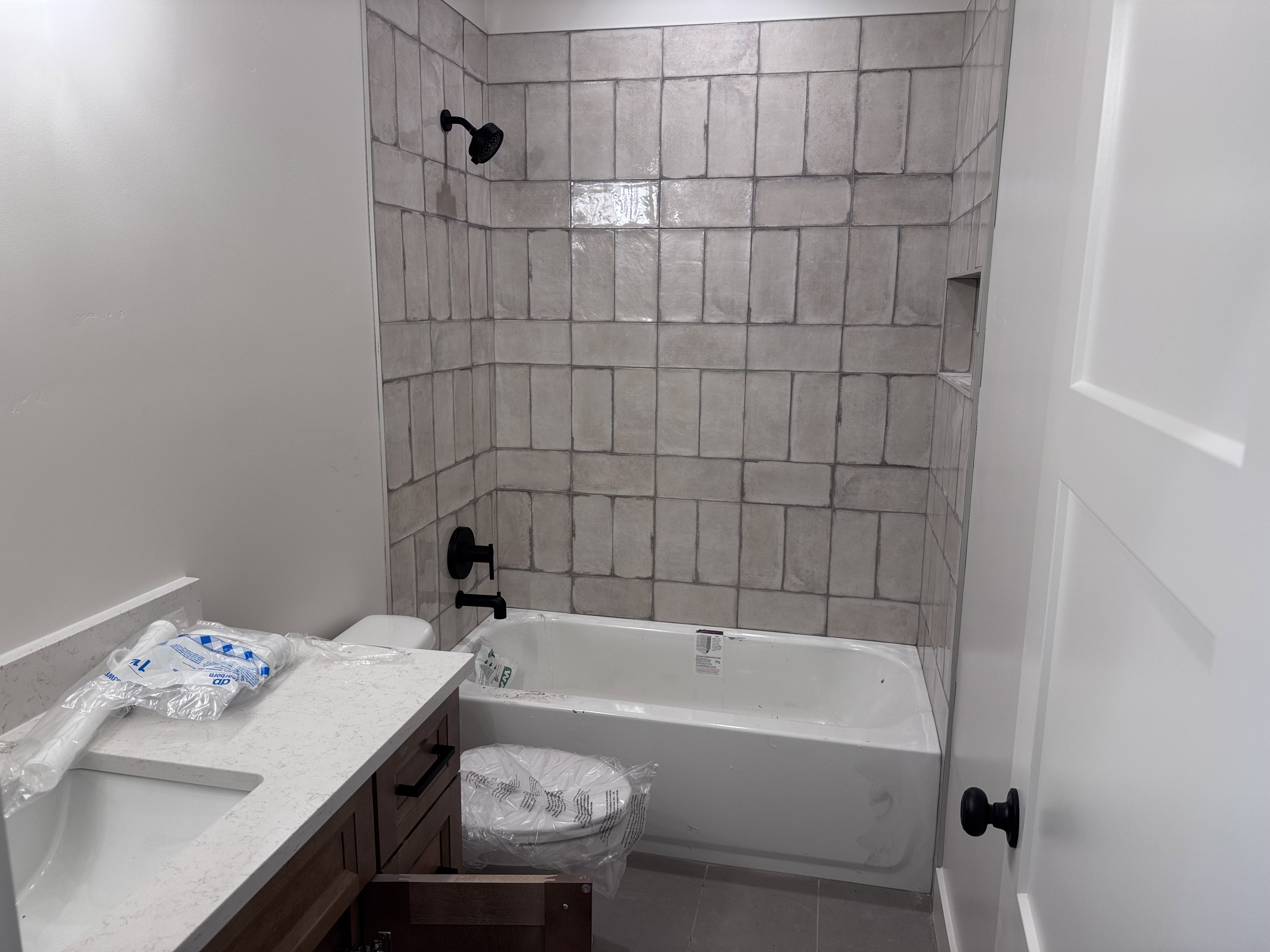 Bathroom featuring a tiled tub surround with a built-in niche, matte black fixtures, and a white bathtub