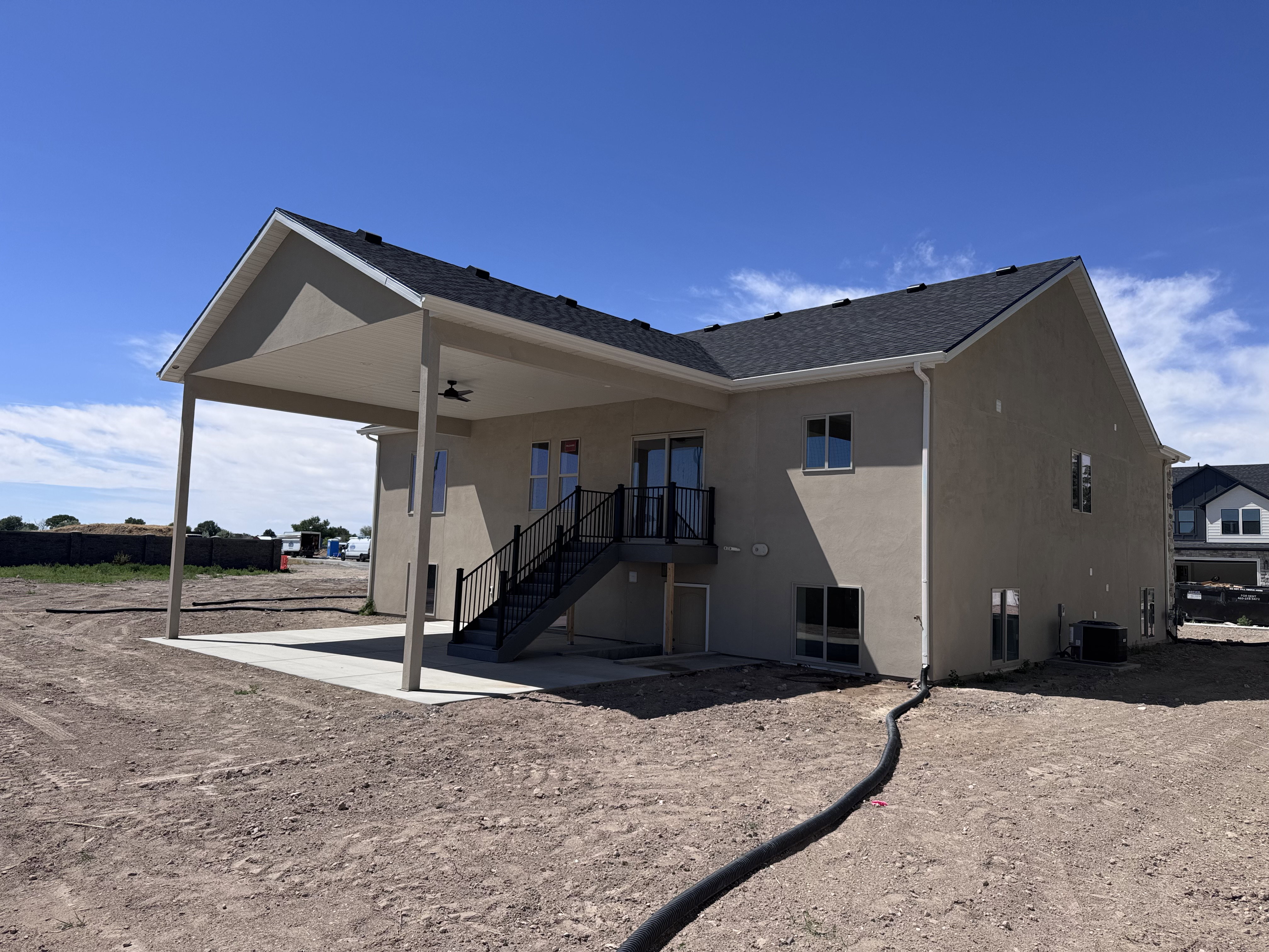 Stucco exterior featuring a covered patio with a ceiling fan, concrete patio, exterior stairs with black railing, and sliding glass doors