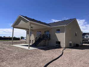 Stucco exterior featuring a covered patio with a ceiling fan, concrete patio, exterior stairs with black railing, and sliding glass doors