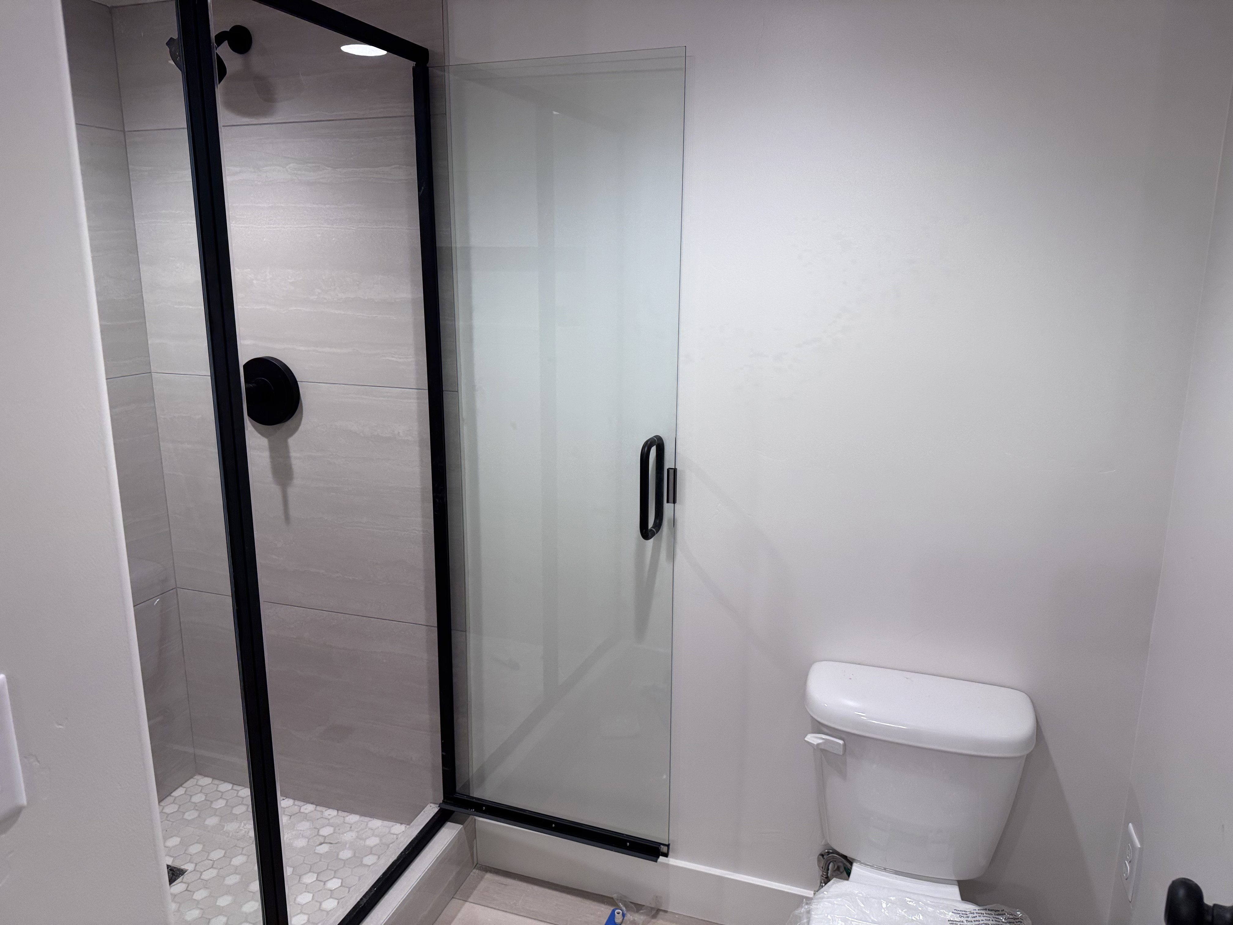 Shower enclosure with matte black framing, clear glass panel, and a matte black shower head and control