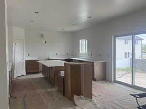 Spacious kitchen featuring an expansive island, U-shaped cabinetry with white countertops, recessed lighting, and a sliding glass door to the exterior