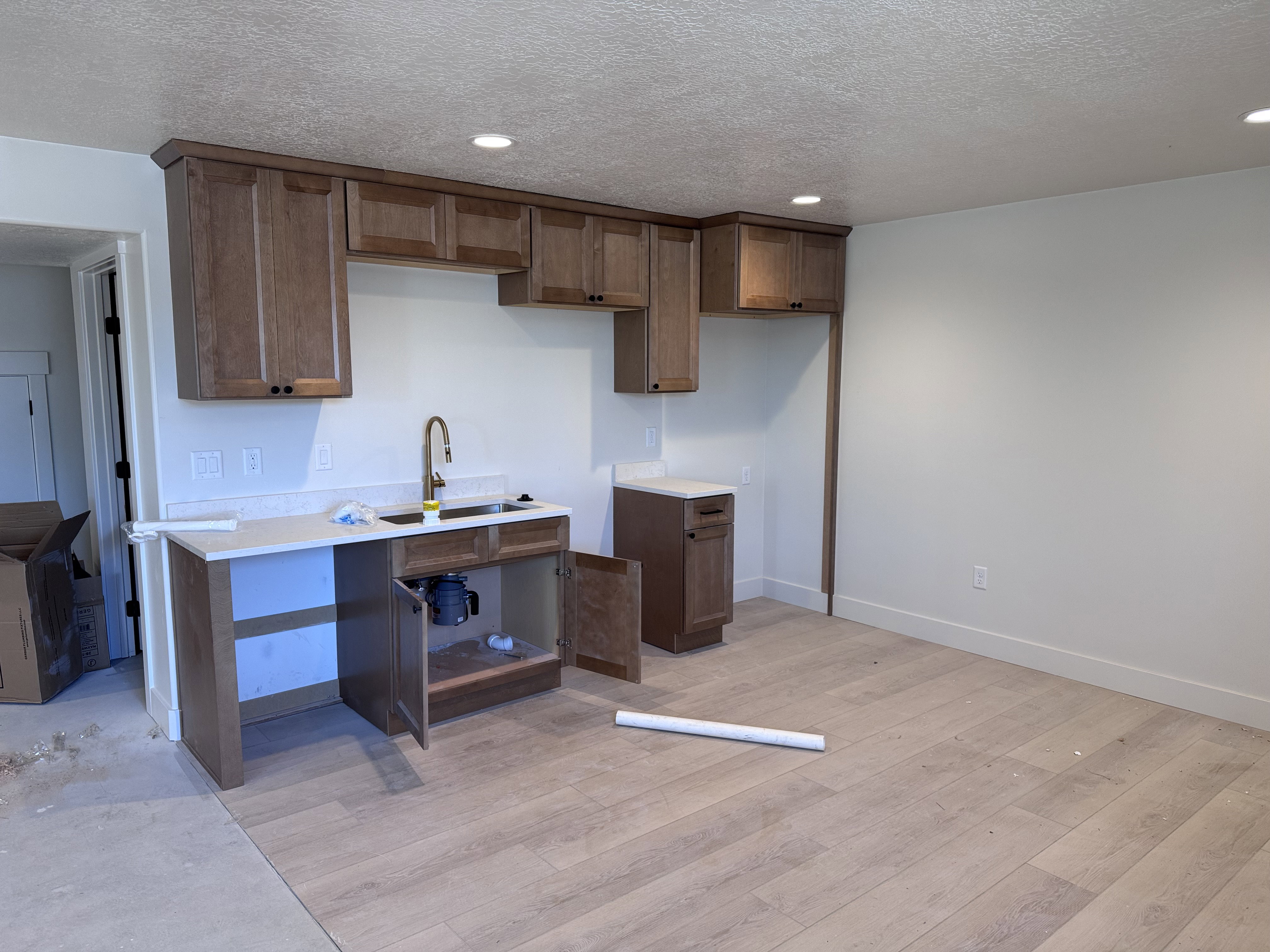 Kitchenette featuring light wood-finish cabinetry, a single basin sink with a bronze-finish faucet, and light-toned countertops