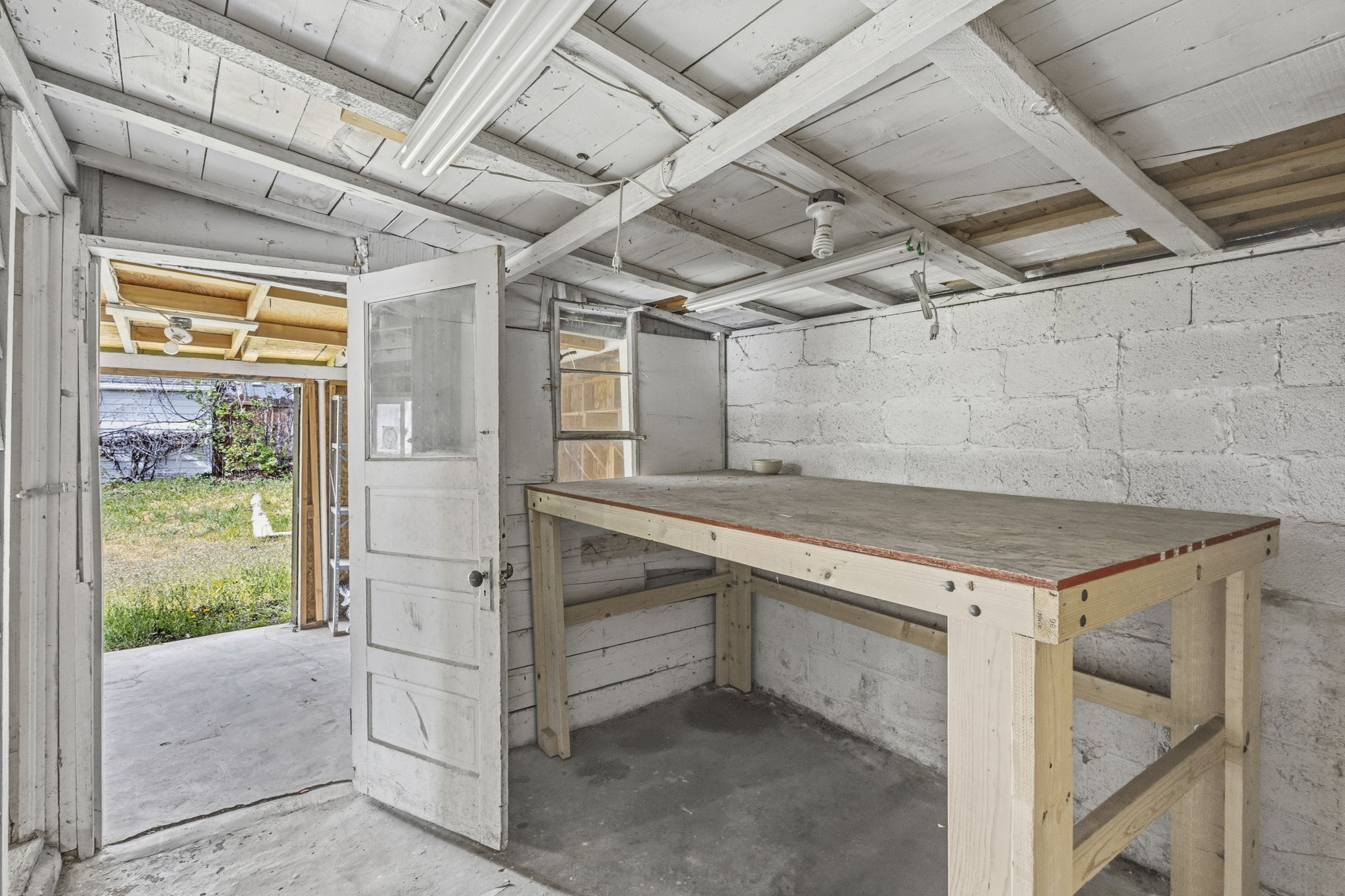 Freestanding structure featuring a concrete floor, painted block walls, exposed ceiling joists, and a built-in workbench
