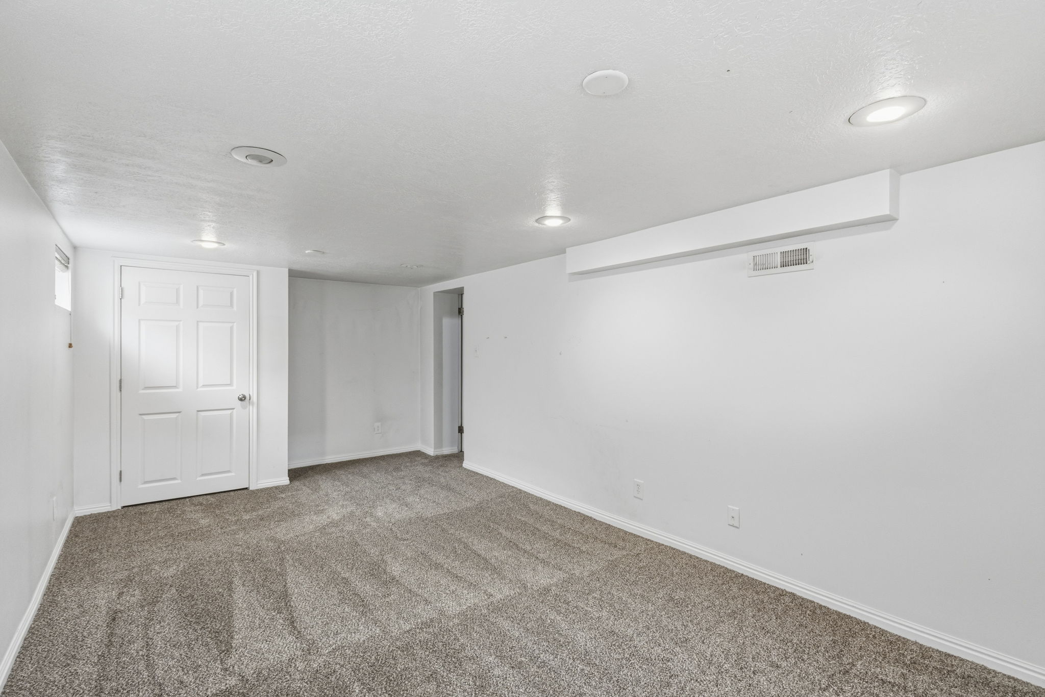 Neutral-toned carpeting spans this spacious room, complemented by white walls and a white six-panel door