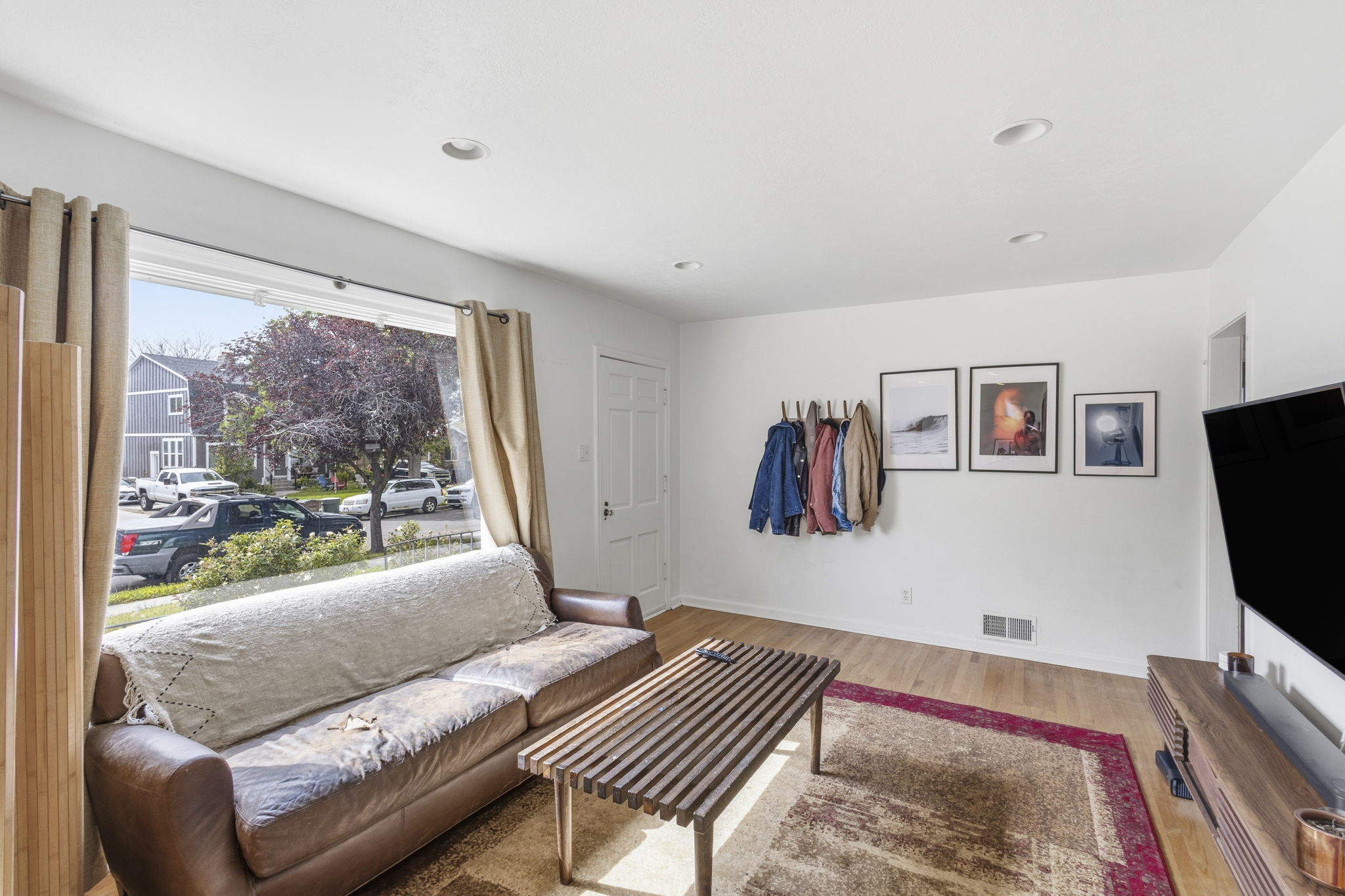 Living area featuring a large picture window, light wood-finish flooring, recessed lighting, and a white paneled entry door
