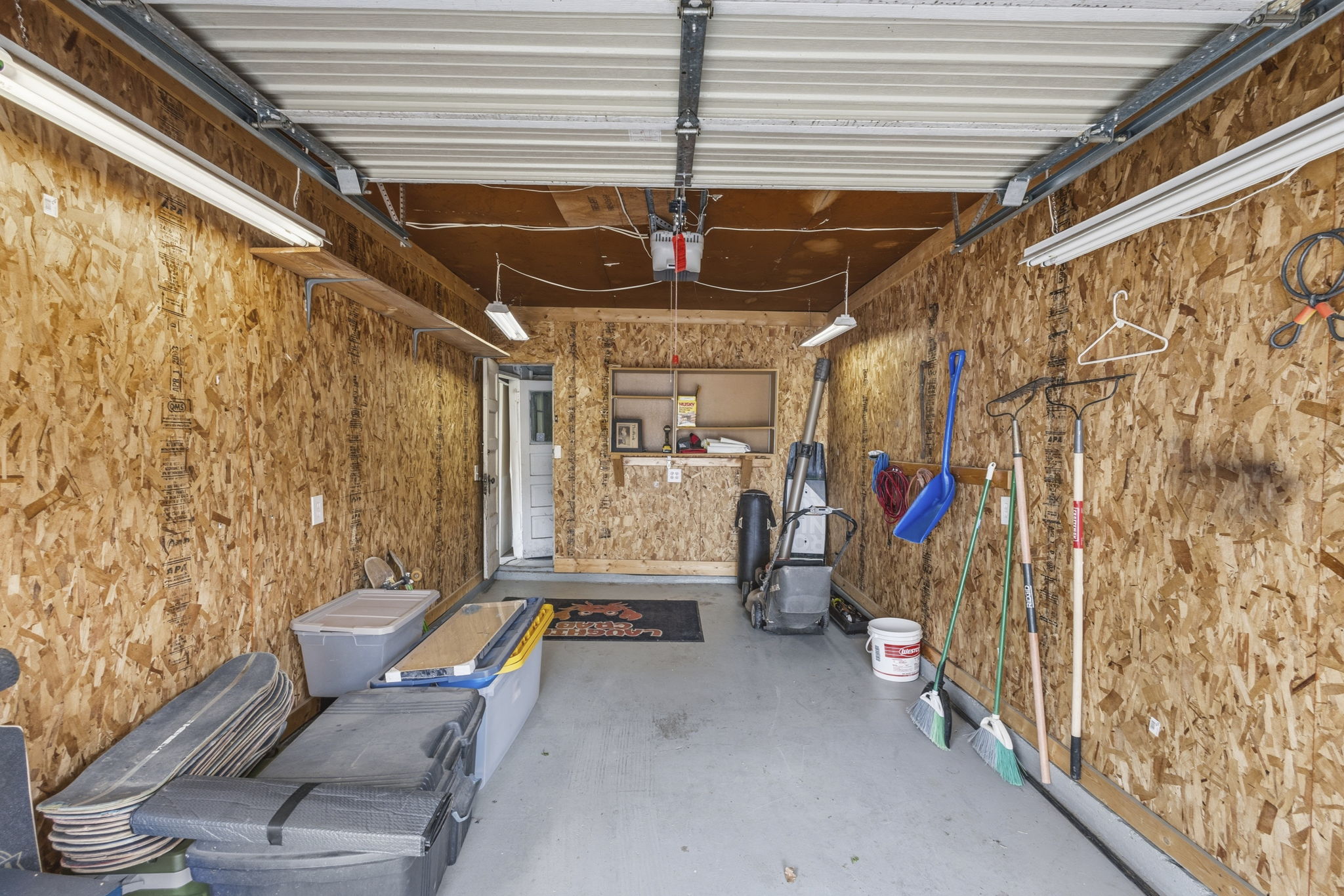 Garage space featuring wood-finish wall panels, overhead fluorescent lighting, and a painted concrete floor