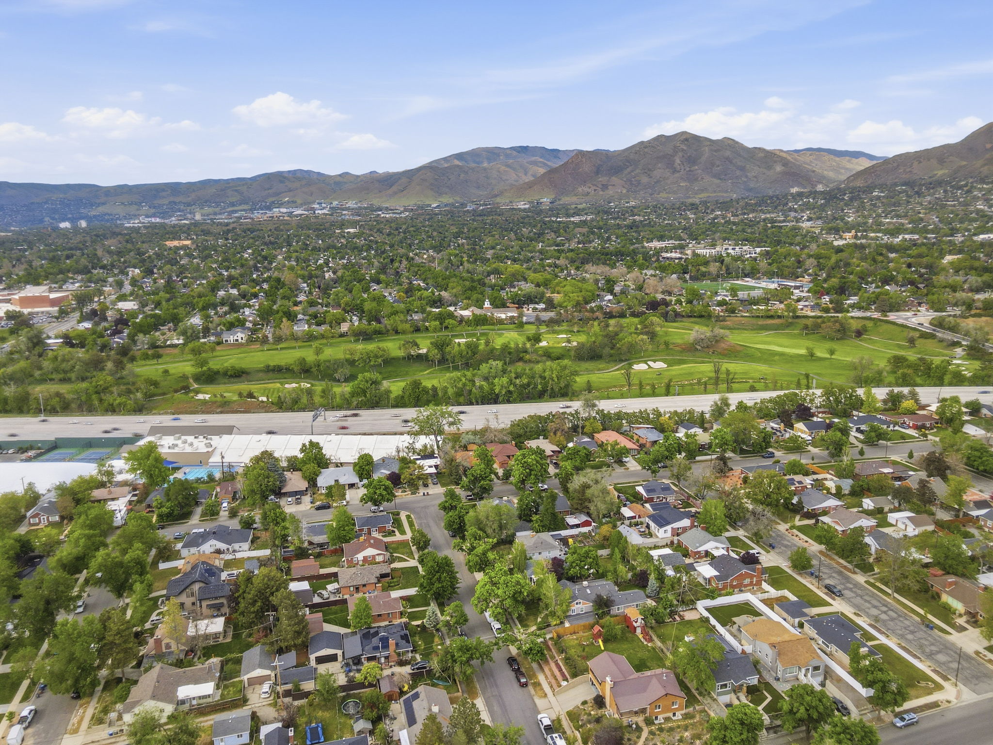 Aerial perspective showcasing a residential neighborhood with tree-lined streets, surrounding green spaces, and distant mountains