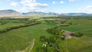 Expansive agricultural landscape featuring verdant fields, scattered trees, and distant mountains under a blue sky with white clouds