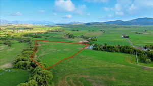 Expansive green pastureland with defined boundaries, bordered by mature trees and distant mountain ranges