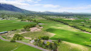 Expansive rural property featuring multiple structures, verdant fields, a paved road, and distant mountain ranges