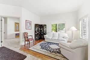 Spacious interior featuring a combination of tile and wood-finish flooring, white walls, and multiple windows with plantation shutters