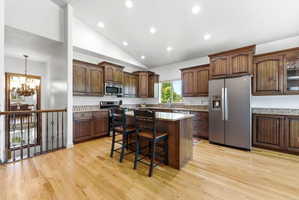 Kitchen with hardwood flooring, vaulted ceiling with recessed lighting, and a multi-level island with seating