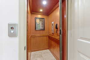 Residential elevator featuring wood paneling, recessed lighting, tile flooring, and a built-in control panel with an emergency phone