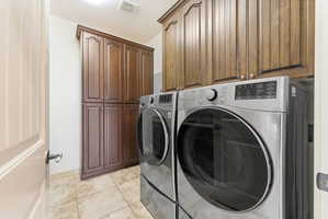 Dedicated laundry space featuring matching front-loading machines, custom wood cabinetry, a built-in storage pantry, and light-toned tile flooring