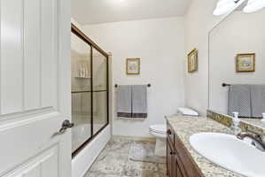 Bathroom featuring a bathtub with sliding glass doors, a vanity with a granite-finish countertop, an undermount sink, and tile flooring