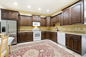 Spacious kitchen featuring dark wood cabinetry, light-toned countertops, and a full suite of appliances including a stainless steel refrigerator, white range, microwave, and dishwasher