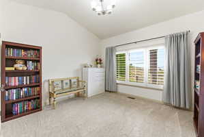 Vaulted ceiling room featuring light neutral carpeting and a three-panel window with plantation shutters