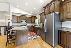 Kitchen featuring wood-finish cabinetry, stainless steel appliances, granite countertops, and hardwood flooring