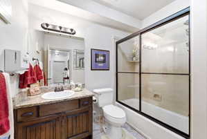 Bathroom featuring a wood-finish vanity with an undermount sink, granite countertop, and a shower-tub combination with a sliding glass enclosure