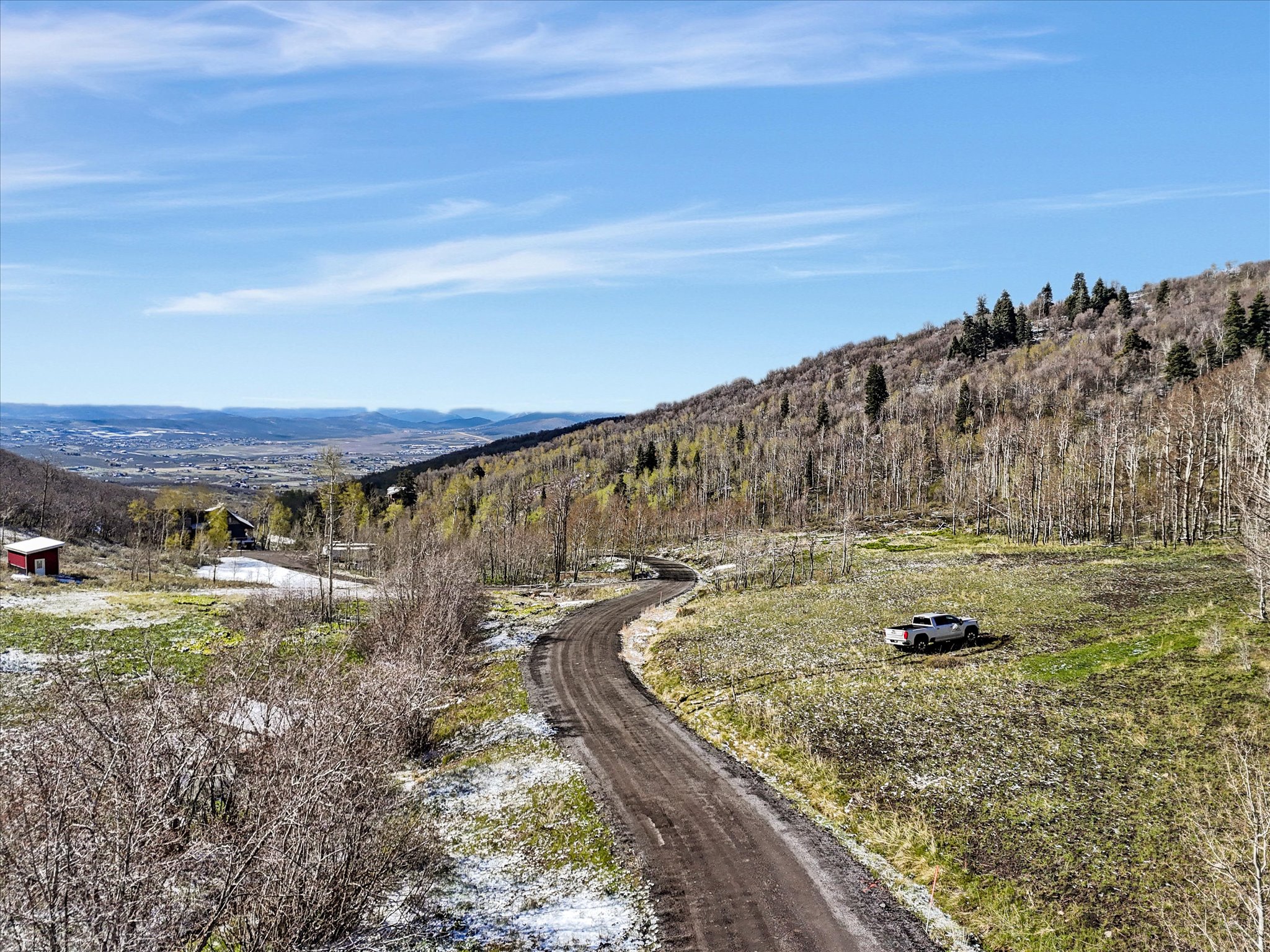 Expansive mountain property featuring a winding dirt road, diverse tree coverage on the hillside, and distant valley scenery