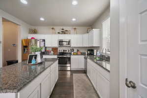 Spacious kitchen featuring an extended island, white cabinetry, recessed lighting, stainless steel appliances, and wood-finish flooring
