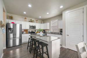 Kitchen featuring a central island with a stone countertop, white cabinetry, integrated stainless steel appliances, recessed ceiling lighting, and wood-finish flooring