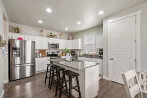 Kitchen featuring a center island with a speckled countertop, white cabinetry, dark wood-finish flooring, recessed lighting, and a stainless steel appliance suite