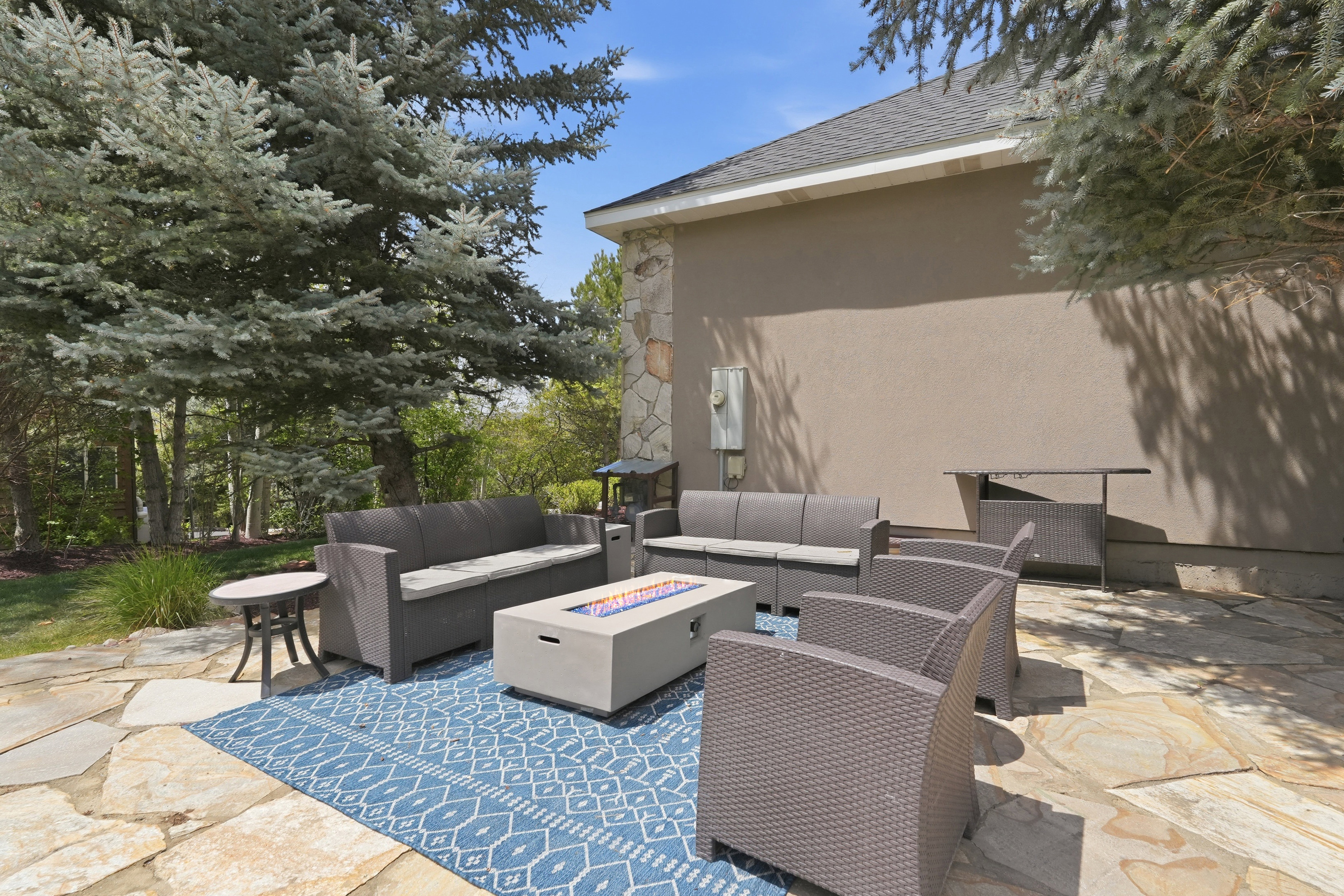 Flagstone patio featuring a fire pit, stucco exterior, stone accent wall, and mature trees