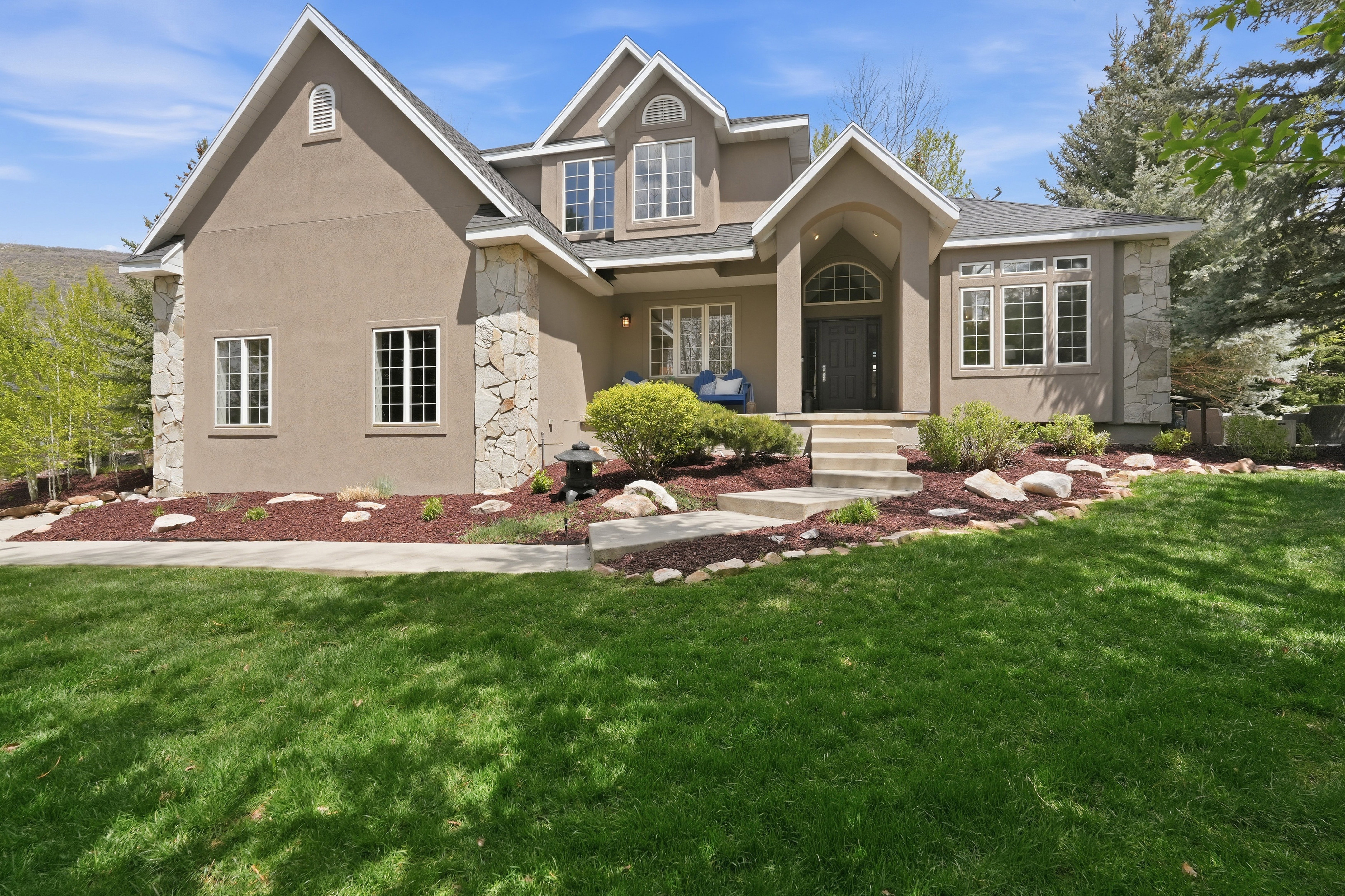 Stucco exterior with stone veneer accents, multiple gables, arched entry, and a large front lawn