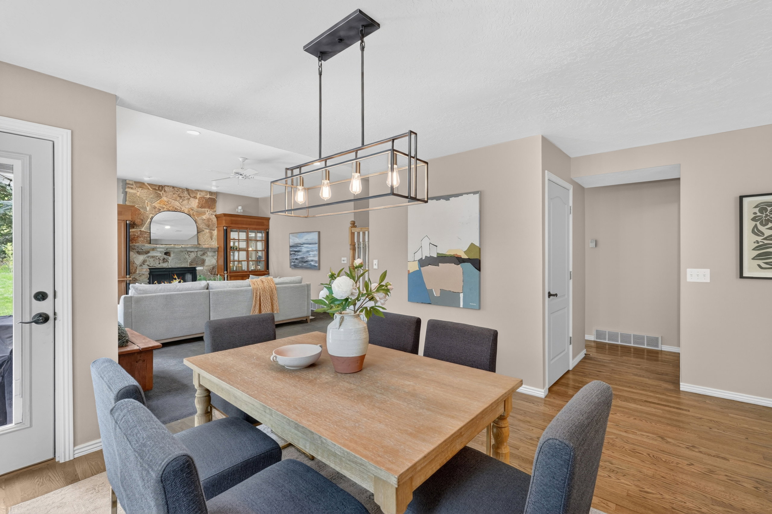 Dining area featuring a wood-finish table with seating for six, an open-concept living space beyond, a decorative light fixture, and hardwood flooring