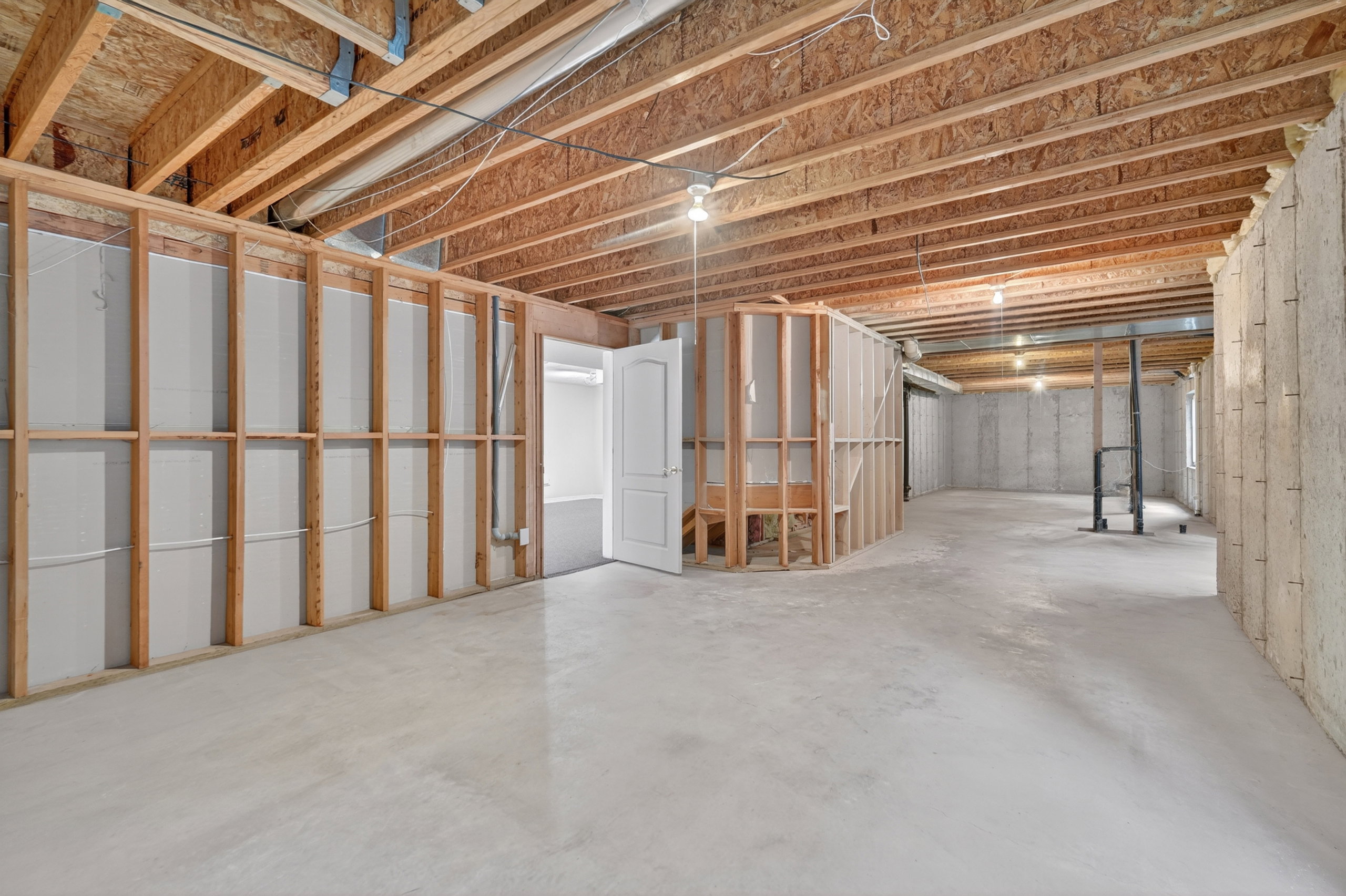 Unfinished lower level with concrete flooring, exposed wood joists, and partial framing for future customization