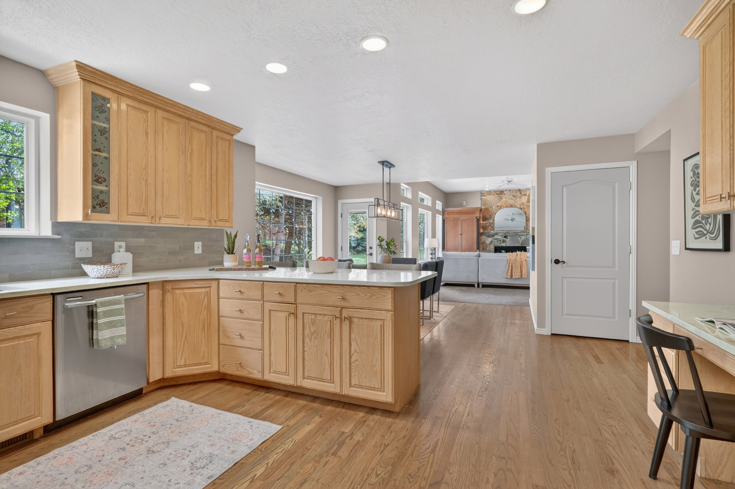 Spacious kitchen featuring wood-finish cabinetry, light countertops, a stainless steel dishwasher, recessed lighting, and wood-finish flooring