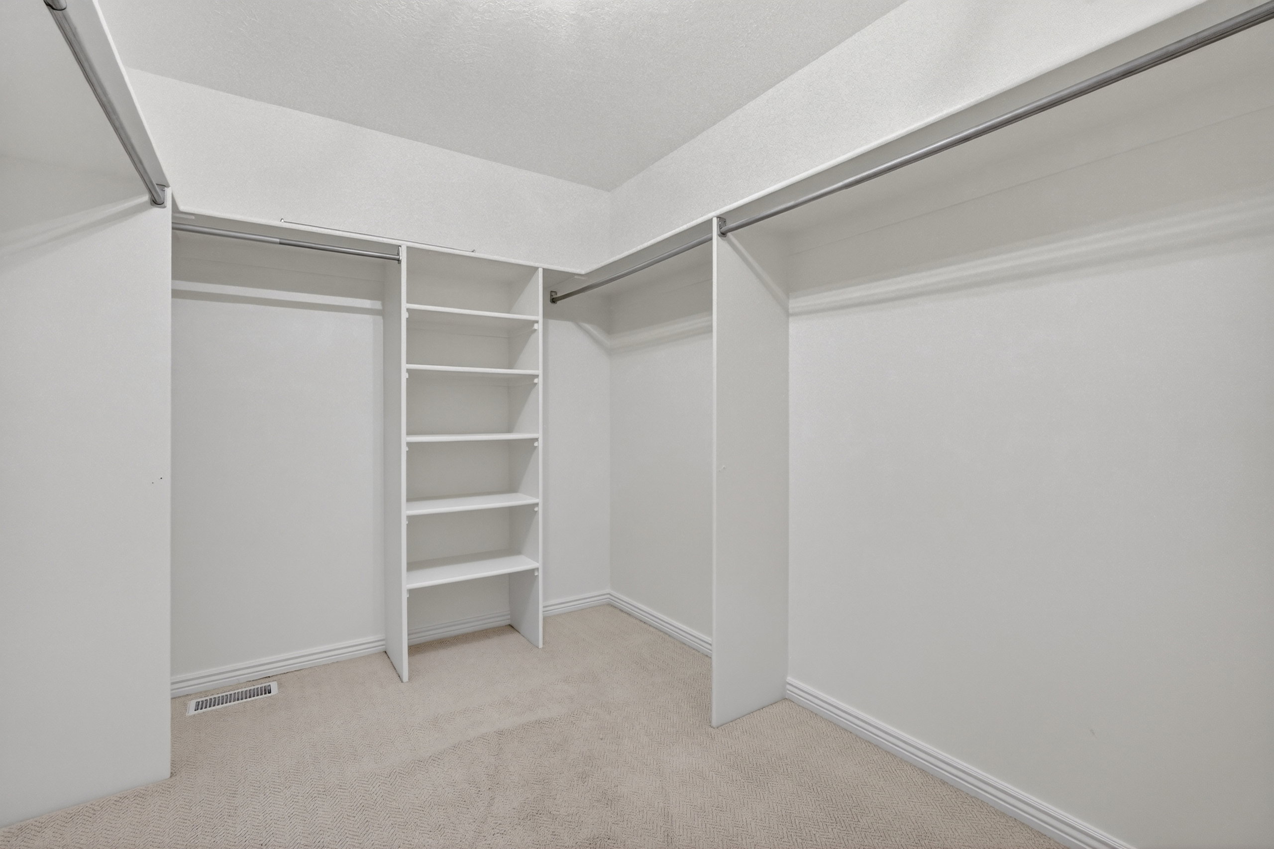 Walk-in closet featuring white built-in shelving, multiple clothing rods, and light-toned carpet flooring