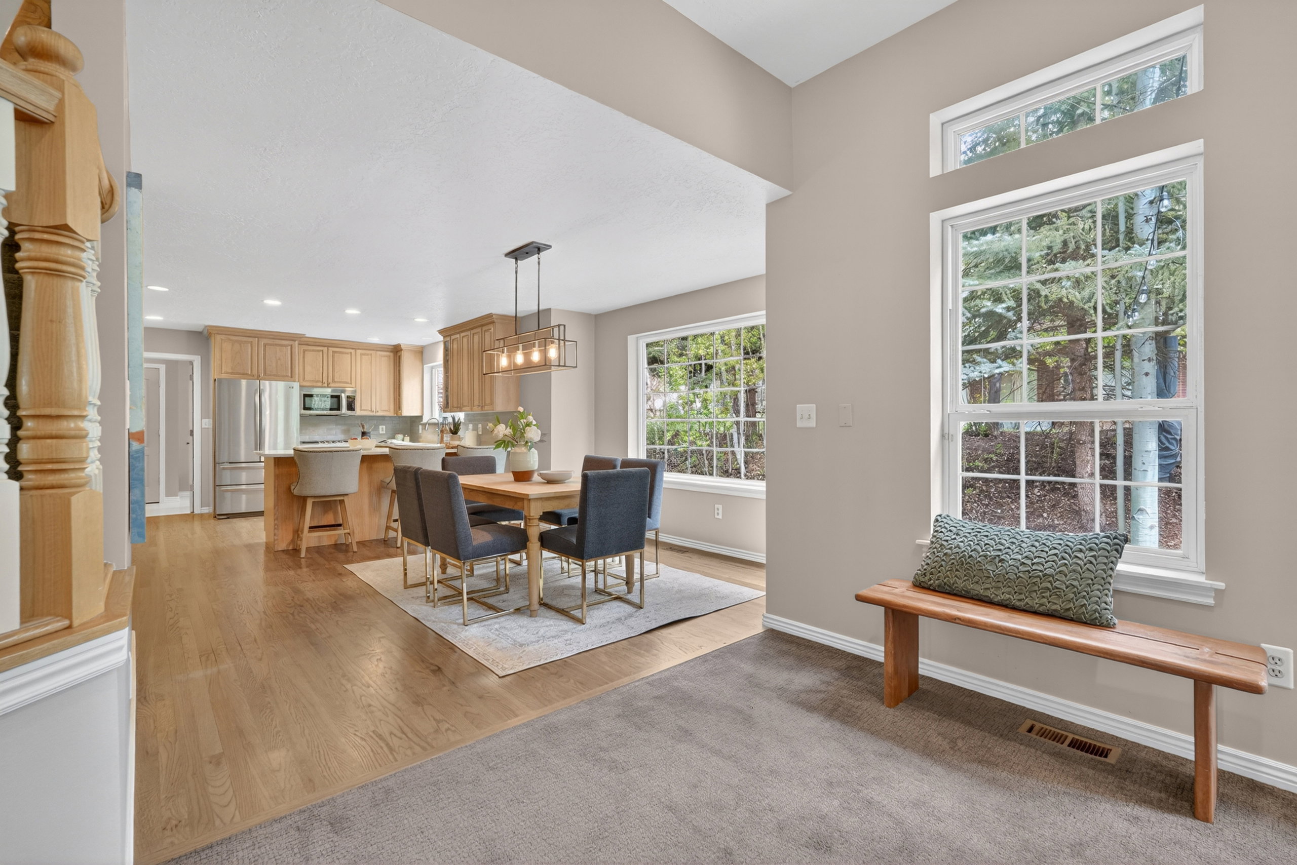 Open-concept kitchen and dining area featuring wood-finish flooring, recessed lighting, a kitchen island with seating, a modern chandelier, and large windows with transom details