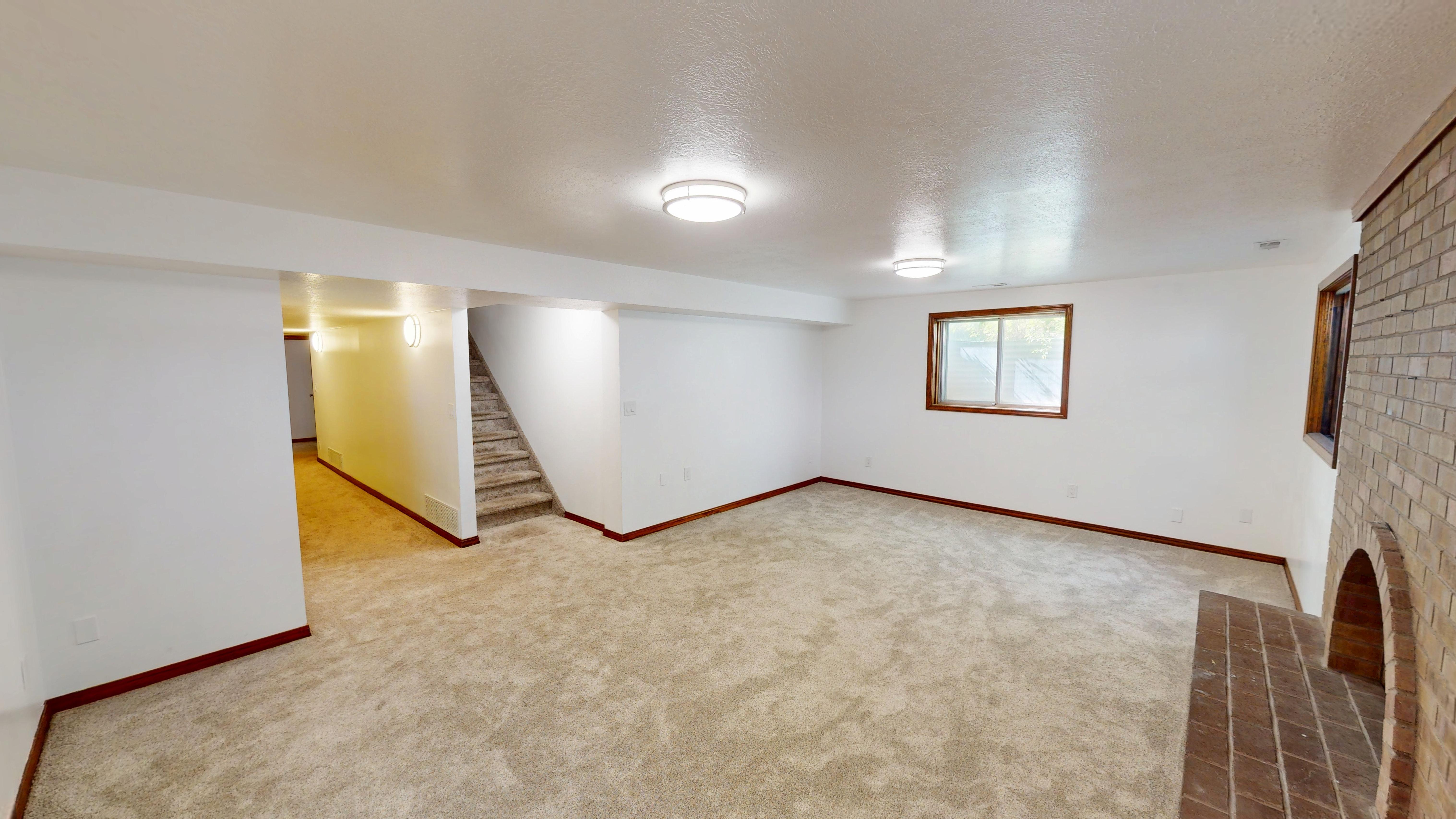 Spacious room featuring light-toned carpeting, white walls, and a brick fireplace