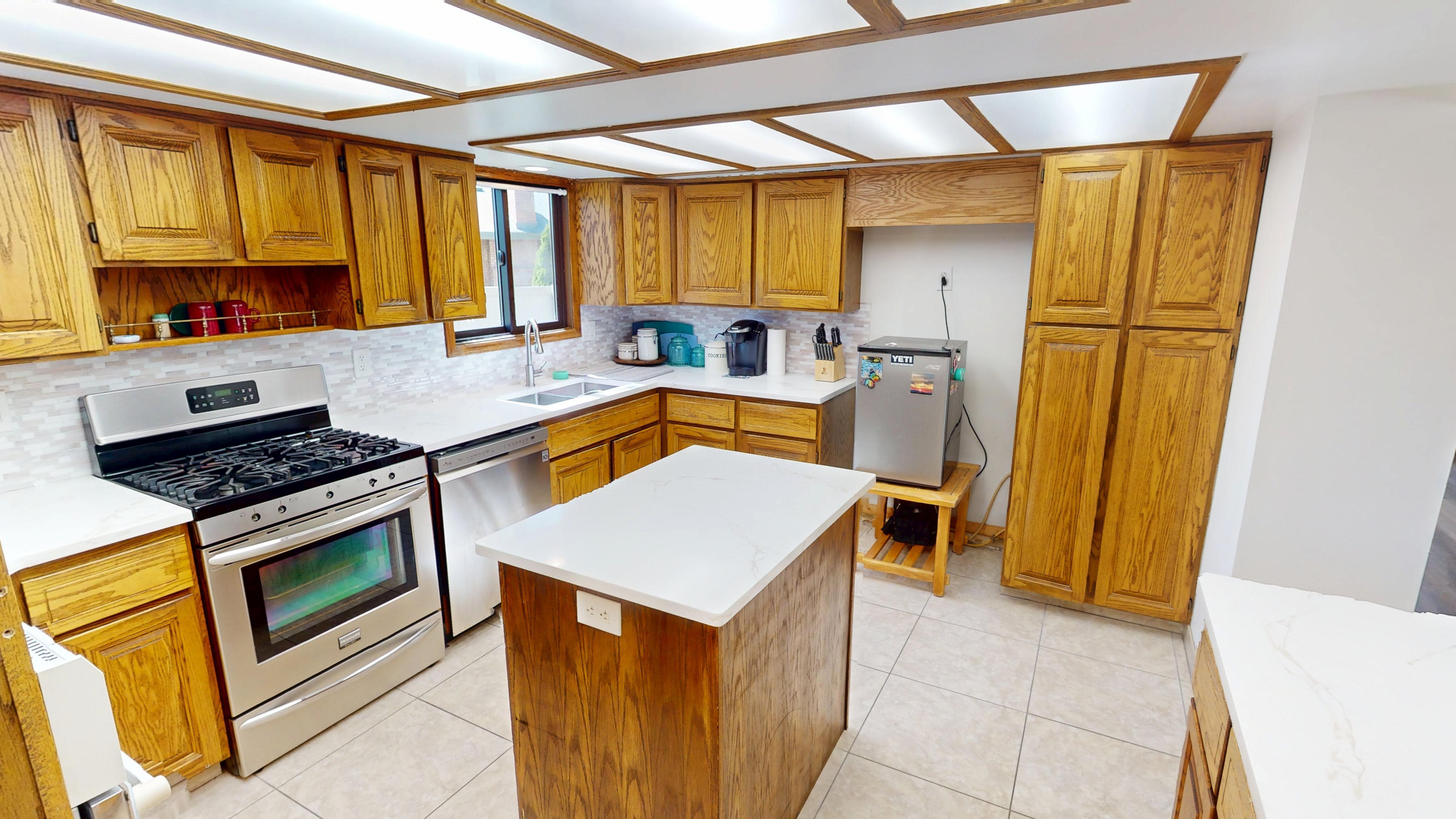 Kitchen featuring wood cabinetry, white countertops, tile flooring, stainless steel appliances, and a central island